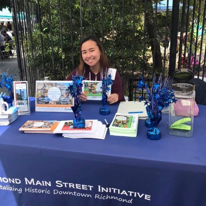 Summer intern Michelle Hong sitting at RMSI info booth, welcoming guests to Healthy Village Festival 2019